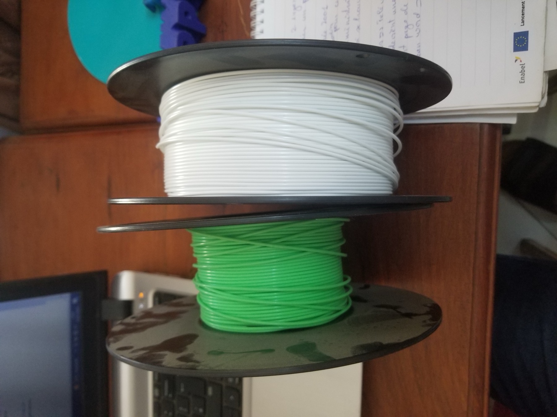 Carretes de PLA blanco y verde apilados en un entorno de trabajo.